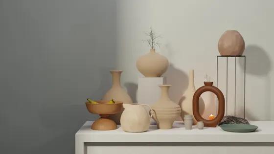 Ceramic vases, fruit bowl and candle arranged on a white plinth