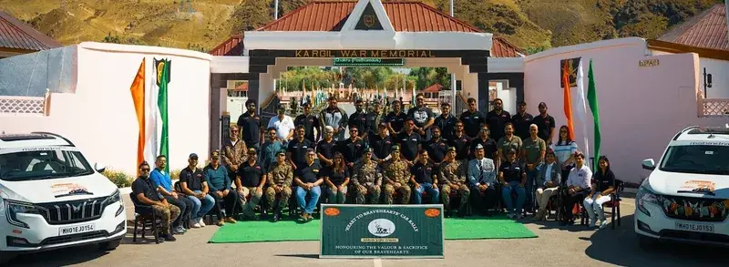 People at the Kargil War Memorial in Dras, with Tololing Peak behind them and two Mahindra SUVs nearby